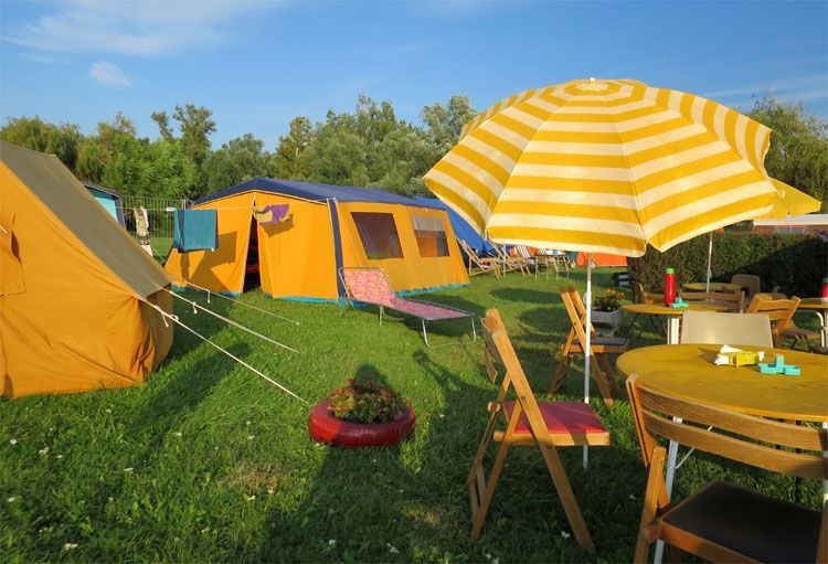 Zeltplatz mit Zelten im Hintergrund und Tisch mit Klappstühlen im Vordergrund
